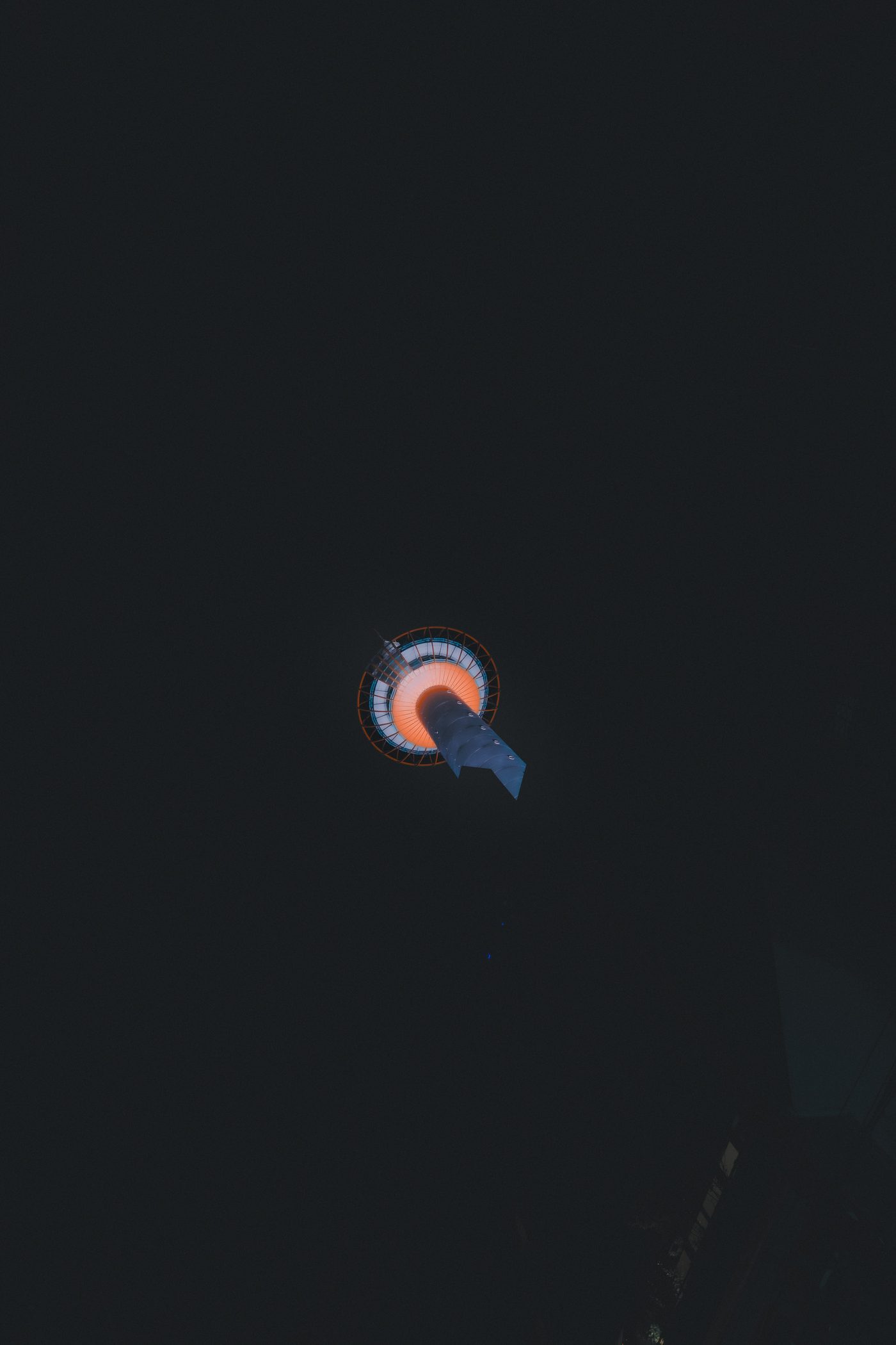 A tower's observation deck hangs high overhead as a small ring of orange and white light, the rest of the frame solid black.